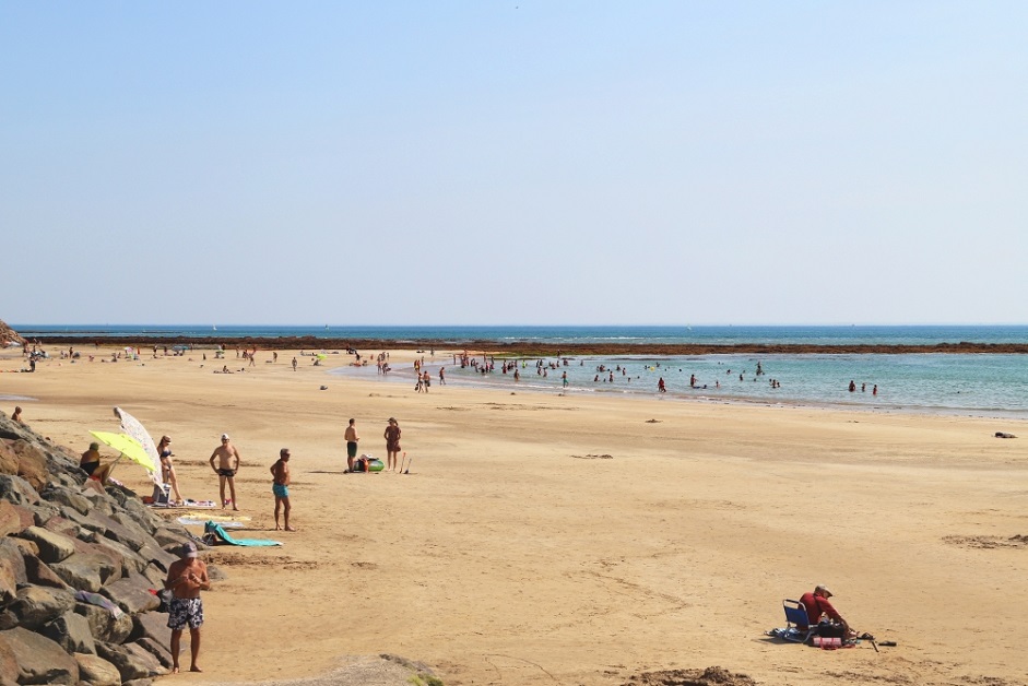 Plage ensoleillée avec des baigneurs et mer calme.