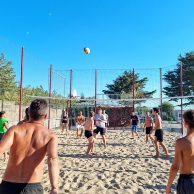 Groupe jouant au volleyball sur sable, ensoleillé.