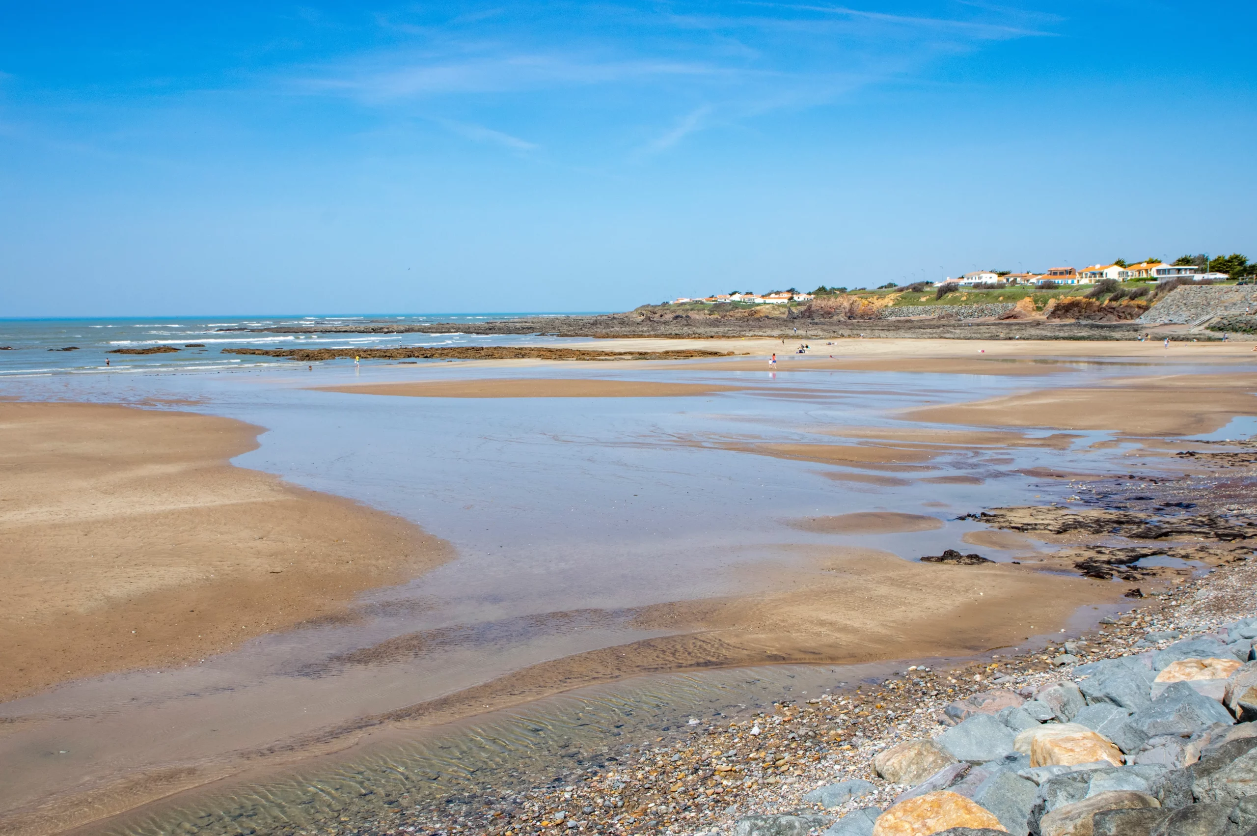 Plage avec mer et rochers sous ciel bleu.